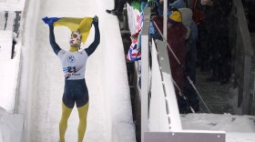 FILE - Vladyslav Heraskevych, of Ukraine, waves a flag as he finishes his second run during the World Cup skeleton competition in Lake Placid, N.Y., Thursday, March 21, 2024. (AP Photo/Seth Wenig, File)