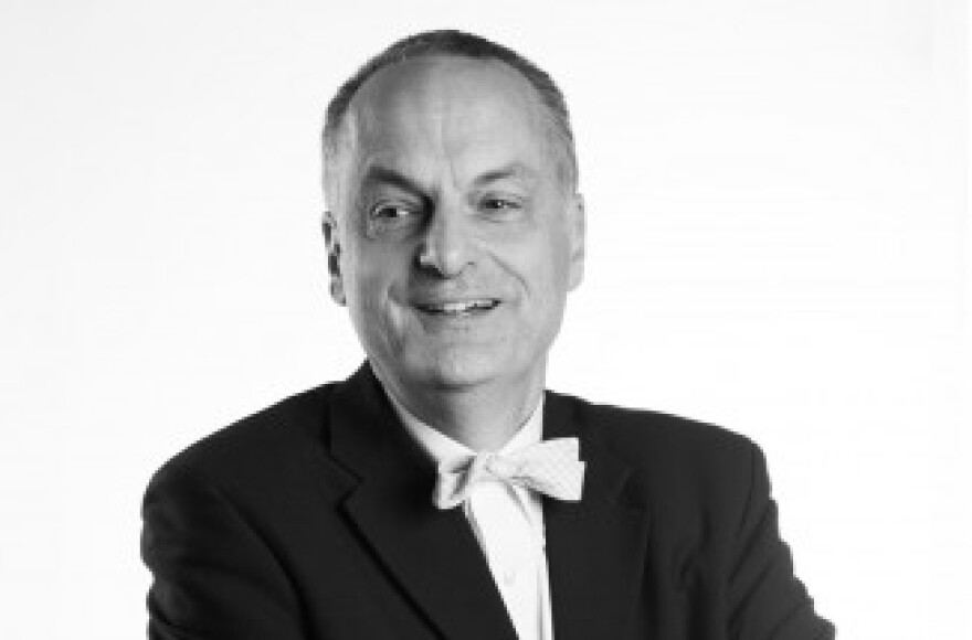 Black-and-white studio portrait of Ed Barry, a smiling man with short gray hair, wearing a black suit jacket, white dress shirt, and white bow tie, photographed against a plain white background.