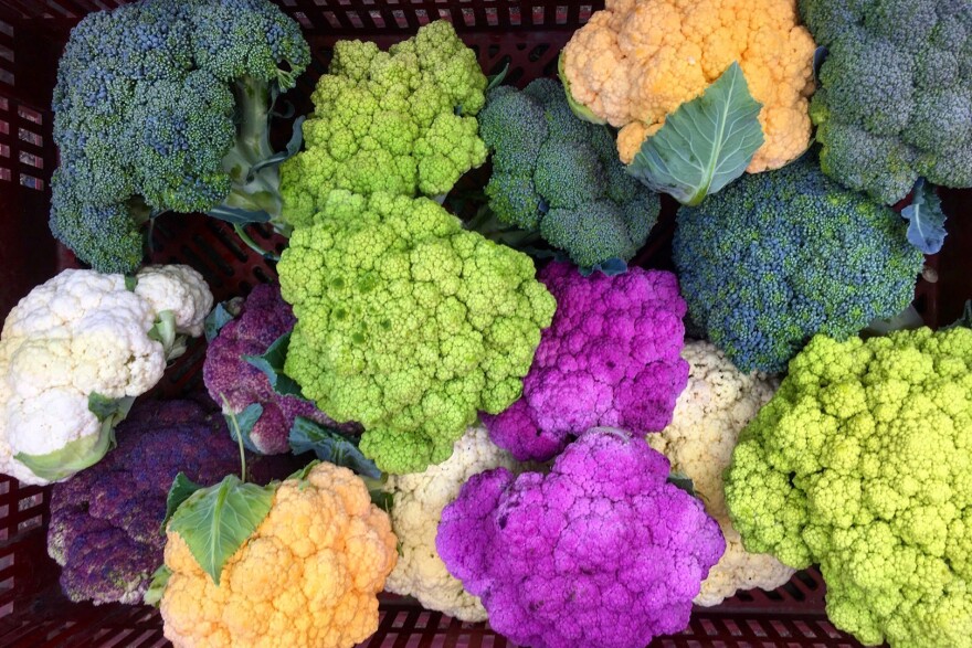 Colorful broccoli and cauliflower sit in a crate.