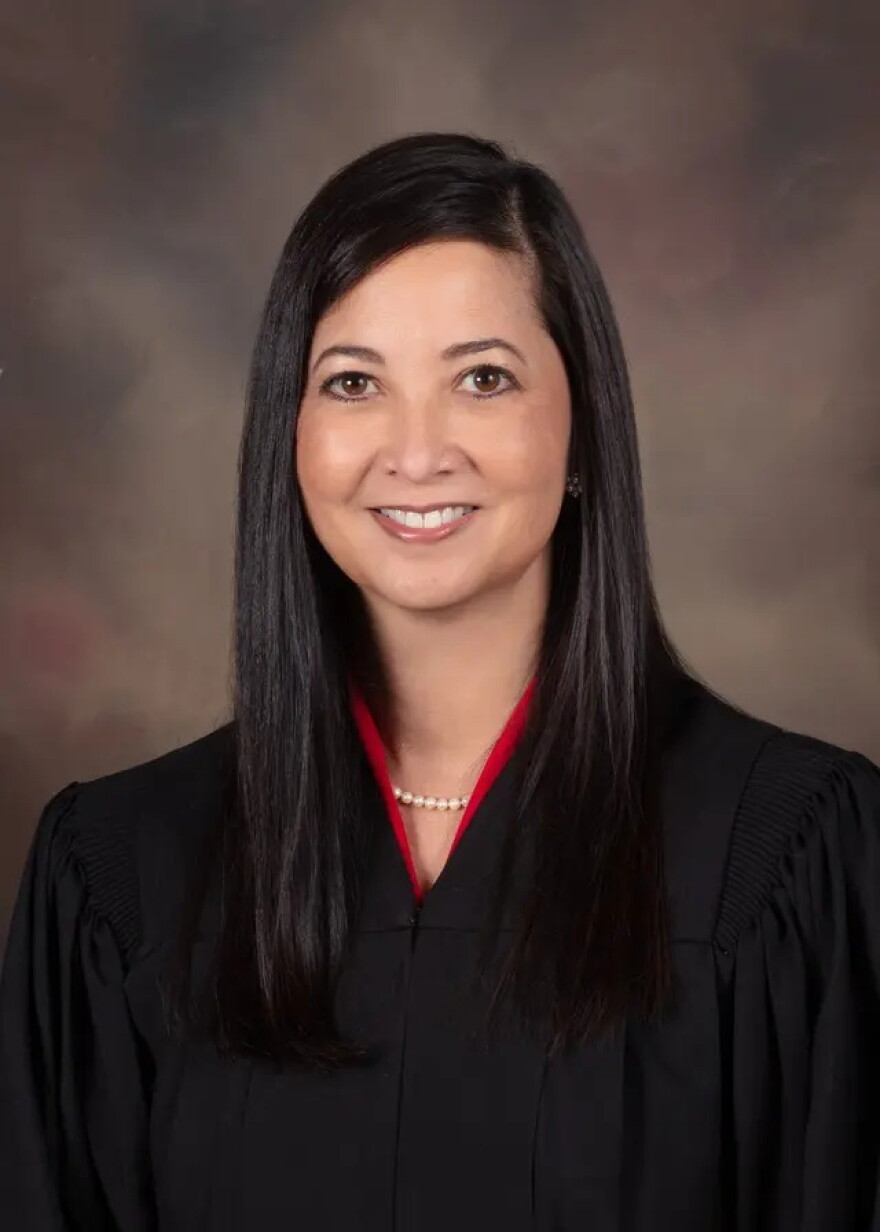 woman with long dark hair sits in a judge's robe