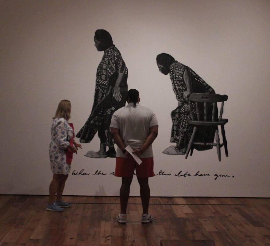 Two visitors view chalk on black paper drawing by artist Chris Friday.