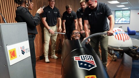 Hassan Williams climbs into the cockpit of the USA Olympic bobsled as Eastman Kodak Company announces its support of USA Bobsled/Skeleton ahead of the 2026 Winter Olympics, unveiling a new state-of-the-art sled in Kodak’s iconic yellow and red at the Golisano Institute for Business & Entrepreneurship. The historic 1956 Bronze Medal–winning “Tyler Sled,” designed and raced by Kodak engineers, was also on display.