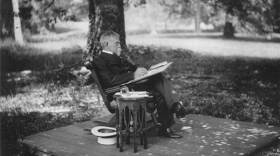 Black and white photograph of author and Civil War general Lew Wallace sitting in a rocking chair on a wooden platform outdoors, writing under a large beech tree.