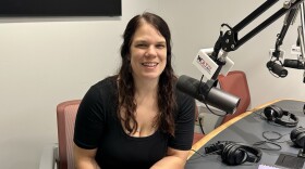 Woman in a black top and seated in a radio studio next to a microphone with a mic flag that reads "WGLT.org 89.1 FM"