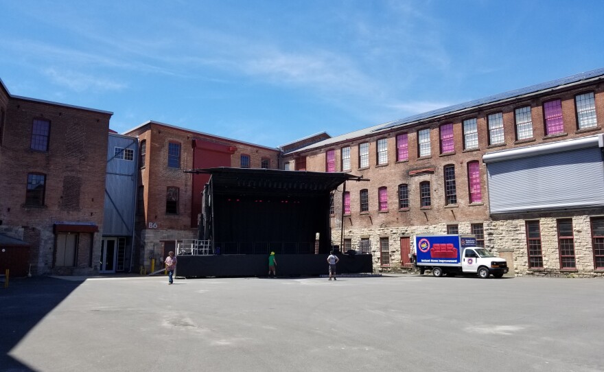 An empty stage sits in an empty brick courtyard with a few people looking at it