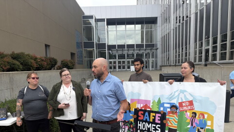 People stand at a press conference in front of a Tacoma court house. They have a banner that reads "Safe Homes For All" 