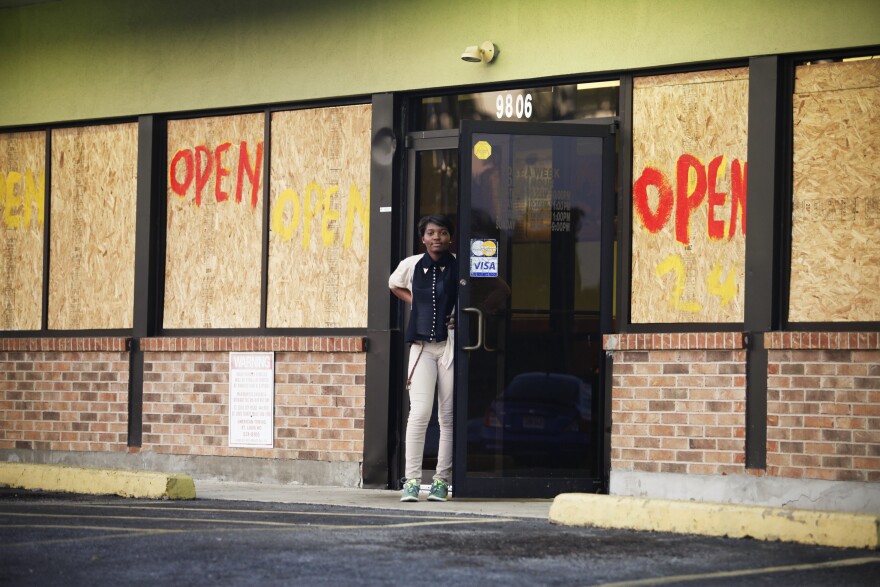 A woman stands before a restaurant on West Florissant Avenue where rioting took place earlier this week. Most of the stores on this stretch are boarded up — some after they were damaged by looters, and some as a precaution — even as many remain open for business.