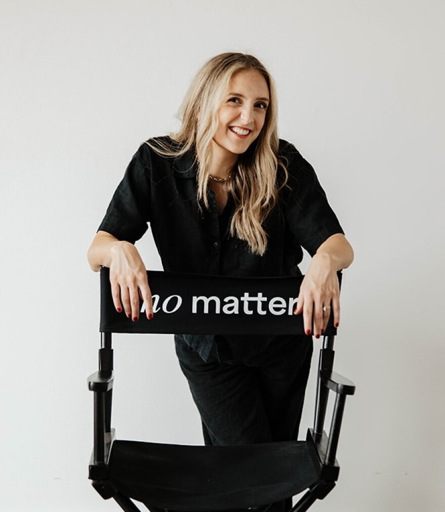 A woman smiles and leans over a director's chair that says "no matter".
