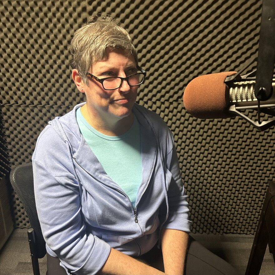 Tracy Adkins, author of Ghosts of Athens: Ghosts of Athens: History and Haunting of Athens, Georgia. A middle-aged, fair-skinned woman with a blonde pixie cut wearing a light-blue zip-up sweatshirt, sitting in a studio with padded walls.