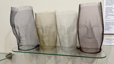 Aluminum wire sculptures of four different heads on a glass shelf and in front of a white wall.