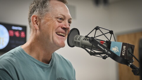 A man wearing a T-shir that reads "No Bad Days" sits inside a radio studio talking at a microphone.