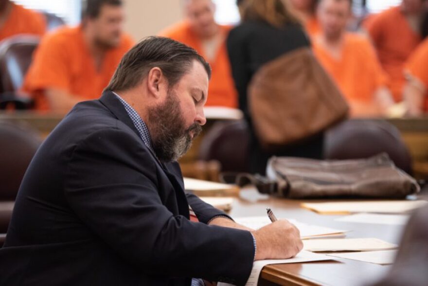 Kevin Finlay, an attorney for the Oklahoma Indigent Defense System, fills out paperwork at a table inside a Cleveland County courtroom on Sept. 26, 2019. Another public defender speaks to defendants in the background.