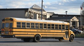 A yellow school bus moves in front of a building that has a sign: Welcome Inn on it. The school bus has "Blue Springs School District" printed on its side.