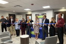 A man holding a large pair of ceremonial scissors cuts a ribbon held by multiple people to open a new building. 