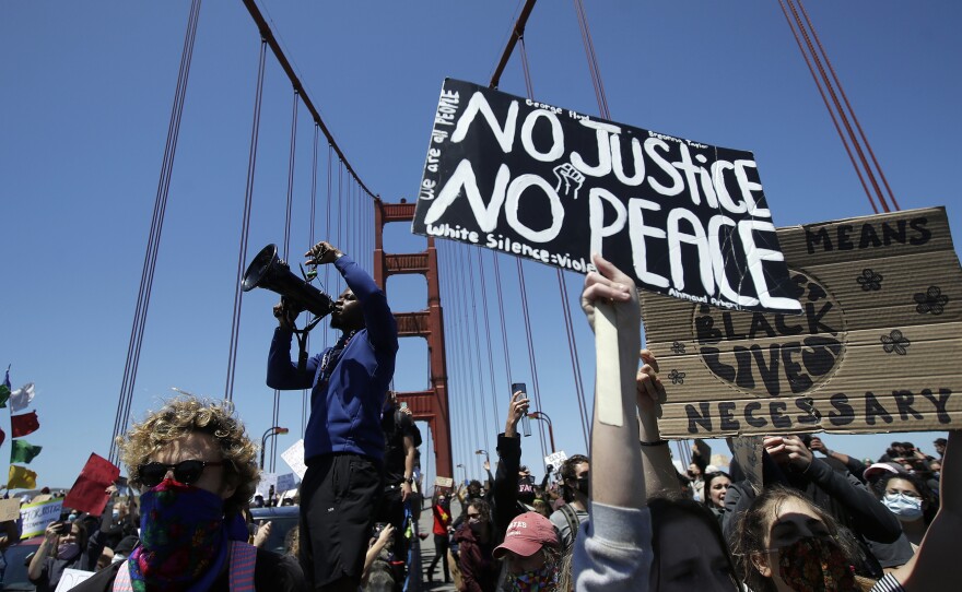 A man speaks into a megaphone while standing with others on the center divider as traffic is stopped on the Golden Gate Bridge in San Francisco Saturday.