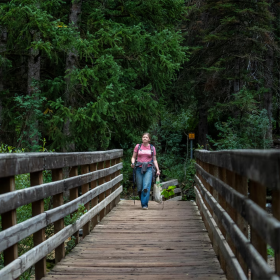 A woman walks down a wooden bridge in a forest.