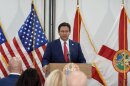 Governor Ron DeSantis speaking at a podium with flags behind him 