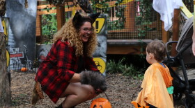 A student dressed as a werewolf hands out candy to a toddler trick-or-treater in the Monster Mash zone at the Santa Fe College Teaching Zoo's Boo at the Zoo event while laughing about their matching baskets on Wednesday, Oct. 28, 2026. (David Caine/WUFT News)