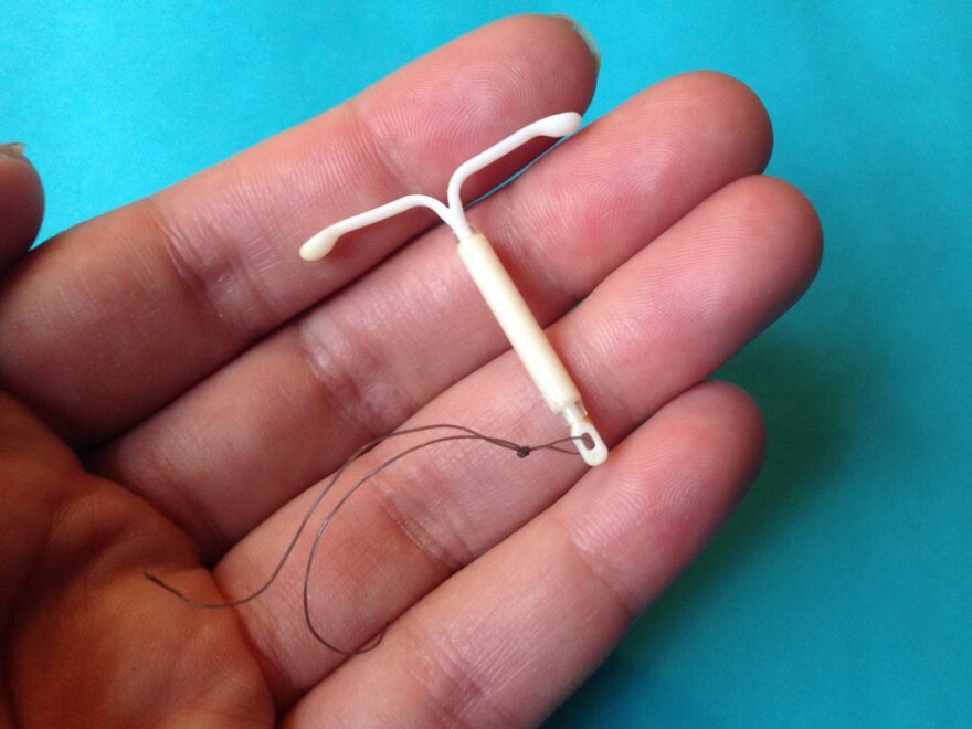 A tan hand holding an IUD.