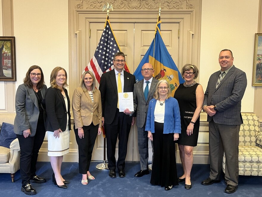Gov. Matt Meyer (center) poses with a smile next to Robert Storch (right) holding a document after his swearing in ceremony. Meyer and Storch's family members stand on either side of them posing with smiles.