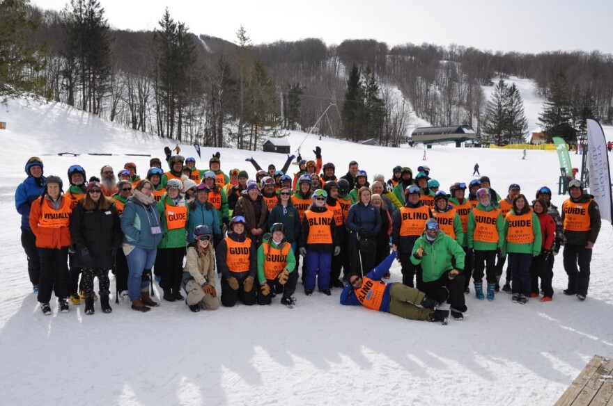 A large group of people in orange vests pose for photo at the bottom of ski mountain