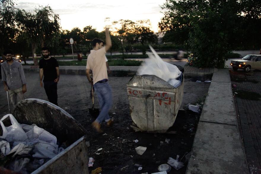 Volunteers throw bags of trash they've collected into a garbage dumpster.