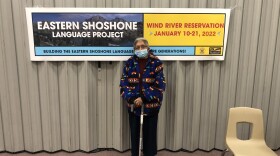 An older woman stands in front of an events banner that says "Eastern Shoshone Language Project"