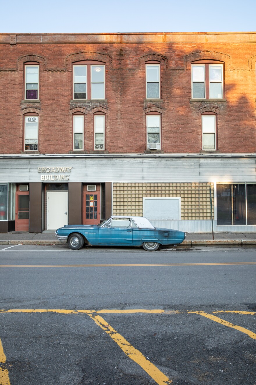 An vintage blue car is parked in front of a brick building in downtown Houlton, Maine. The photo shows the car from the side.