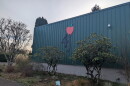 Green outdoor wall with 4J and an apple logo on it. in the foreground bushes and a sidewalk.