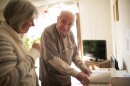 An older gentleman stands in front of a desk and smiles at a woman assisting him. 