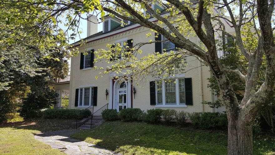 A large yellow house with black shutters and a tree in the foreground.