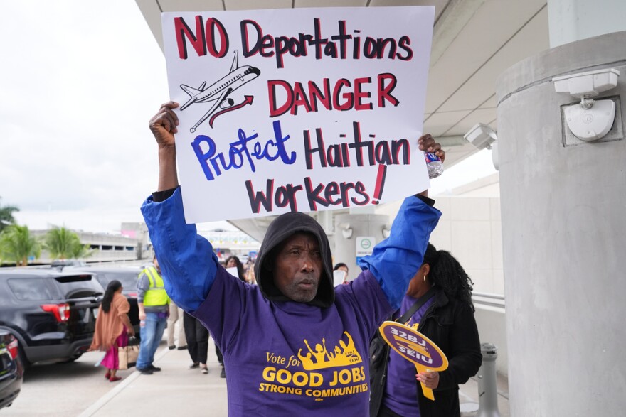 African American man holds sign saying No Deportations, Danger, Protect Haitian Workers 