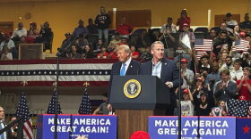 U.S. Sen Jon Husted and President Donald Trump stand on stage together at a rally in Vandalia, Ohio, with a crowd of supporters behind them