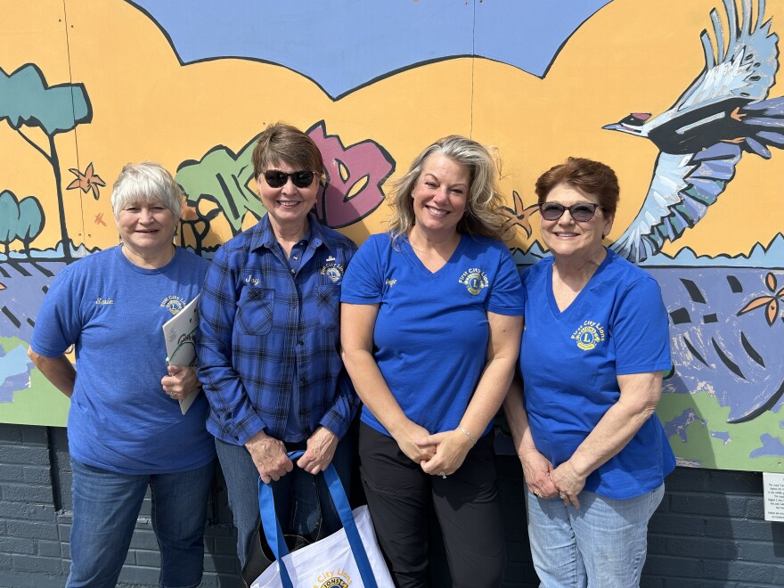 Four women wearing blue standing in front of a mural of wetlands.