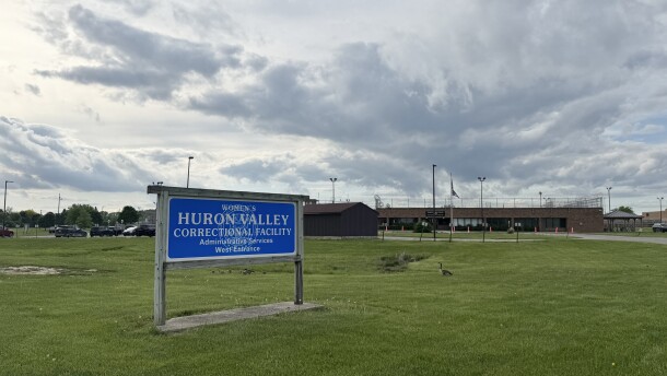A sign outside a prison that says "Women's Huron Valley Correctional Facility" in white text on a blue board.