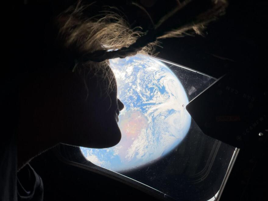 NASA astronaut and Artemis II Mission Specialist Christina Koch peers out of one of the Orion spacecraft's main cabin windows, looking back at Earth, as the crew travels toward the Moon.
