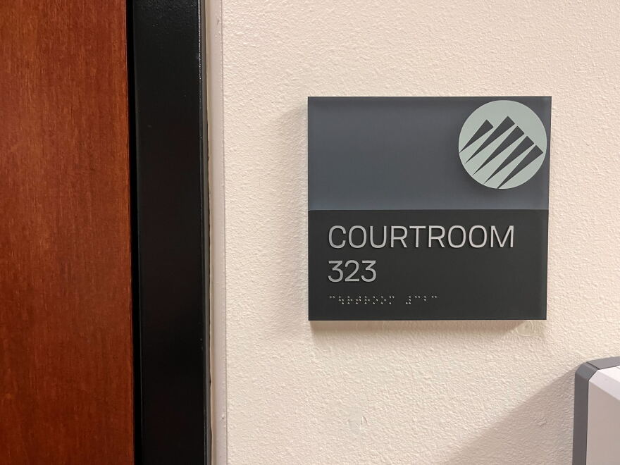 A sign next to a wood door with the Pierce County logo reads "Courtroom 323" in text and Braille.