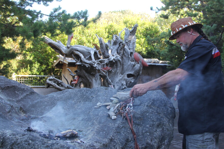 A man holds a burning piece of sage in a secluded garden memorial. 
