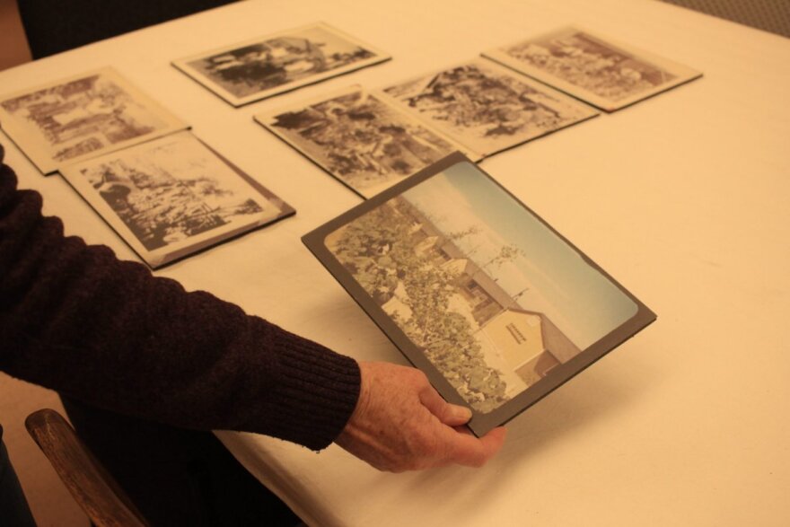 In the second photo, she holds a photo of vegetable gardens — known during wartime as “victory gardens” — planted at the edge of the barracks in Amache.