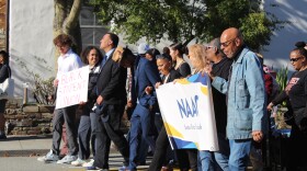 A line of people march together along a street. One sign reads "Black Student Union" and another reads "NAACP Santa Cruz County."