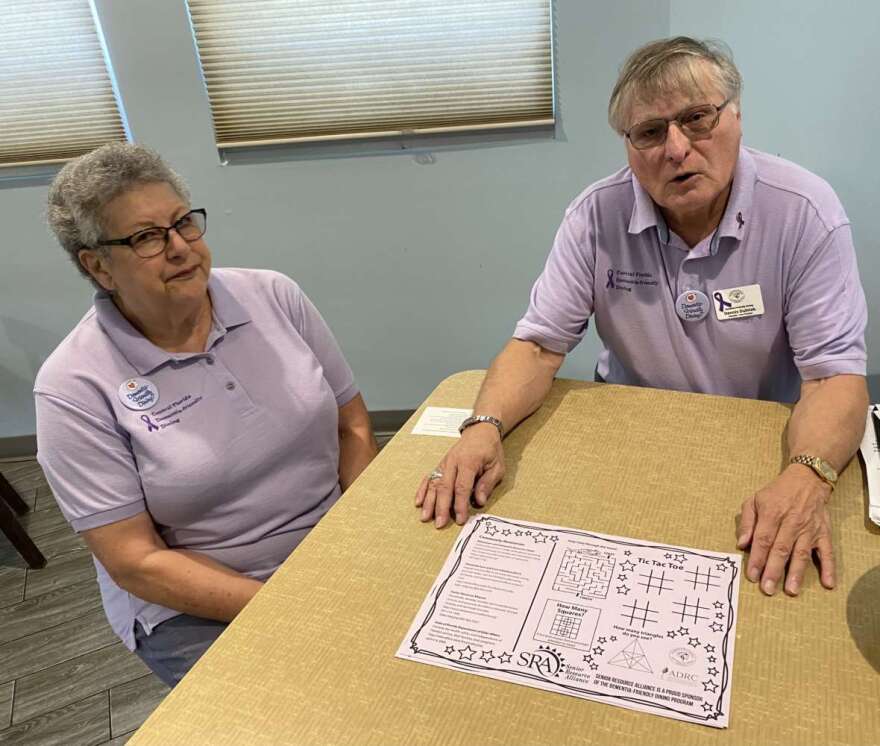 Toni Gitles and Dennis Dulniak describe a place mat with simple puzzles for dinners dealing with dementia and a list of resources. Photo: Joe Byrnes, WMFE News