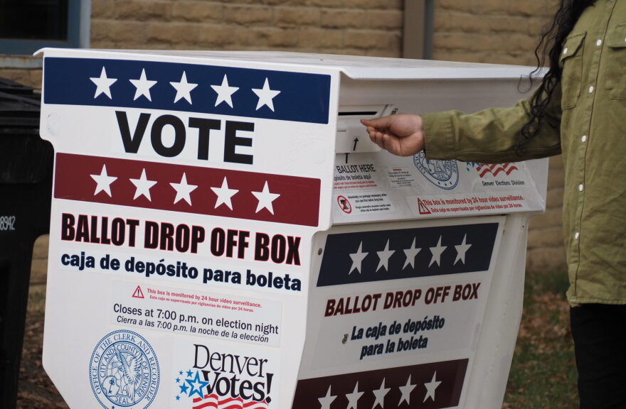 A voter drops off their ballot at a ballot drop box outside that has red white and blue coloring.