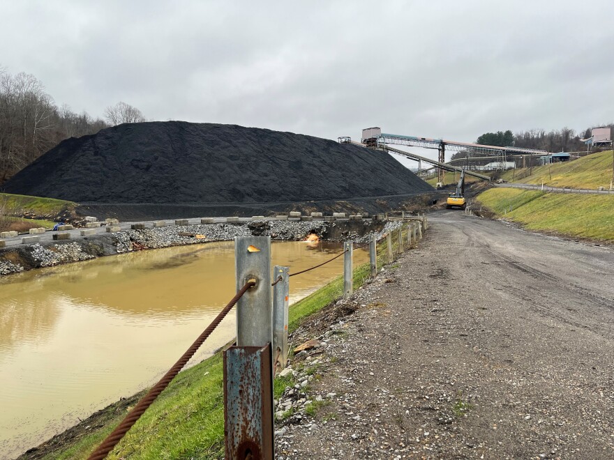  A large pile of coal and an orange-brown colored slurry pond.  A large belt is in the background that transported the cleaned coal down the mountain to a nearby power plant.