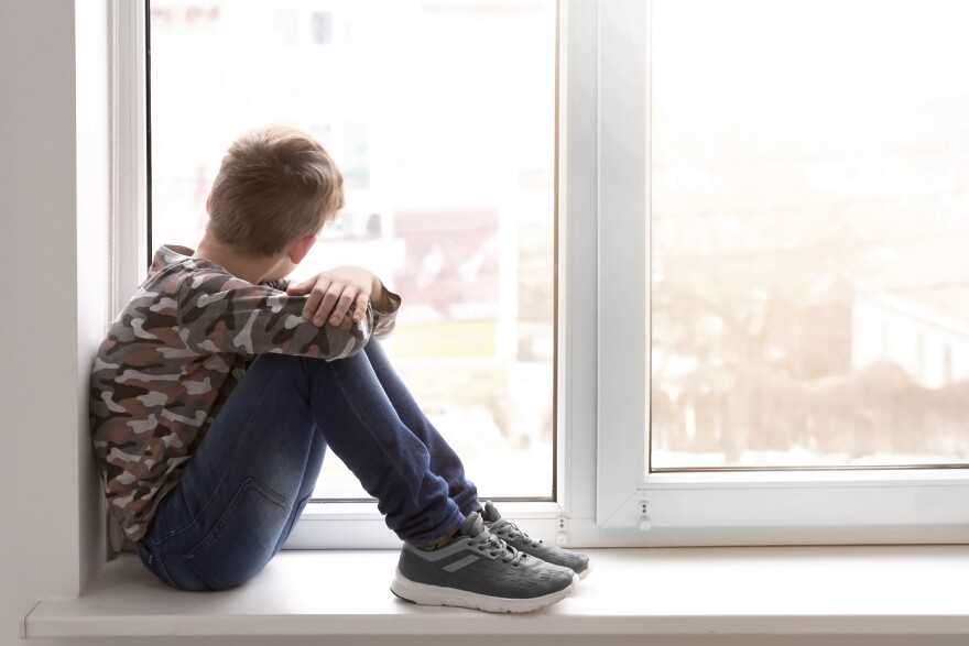 Lonely boy sits near window indoors. 