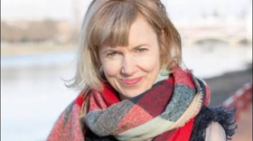 A woman with short blonde hair wears a red, white, and blue scarf and smiles at the camera. 