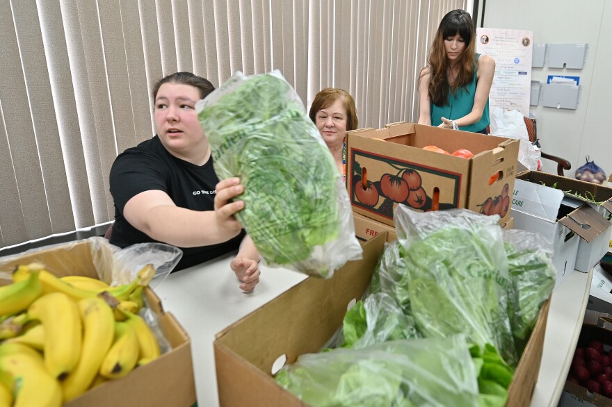 Brynn Gilbert, a National Health Corps’ (NHC) Community Health Fellow, grabs a head of lettuce to be packed for Volunteers in Medicine clients, as Mary Theresa Mazur, the fellowship's program director, looks on. Elsa Romero, also a fellow, packs bags of fresh fruits and vegetables.