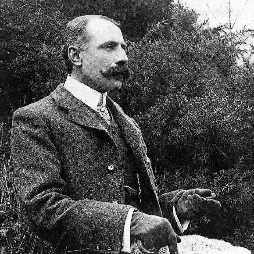 Edward Elgar sits outside wearing a tweed suit and sporting a mustache