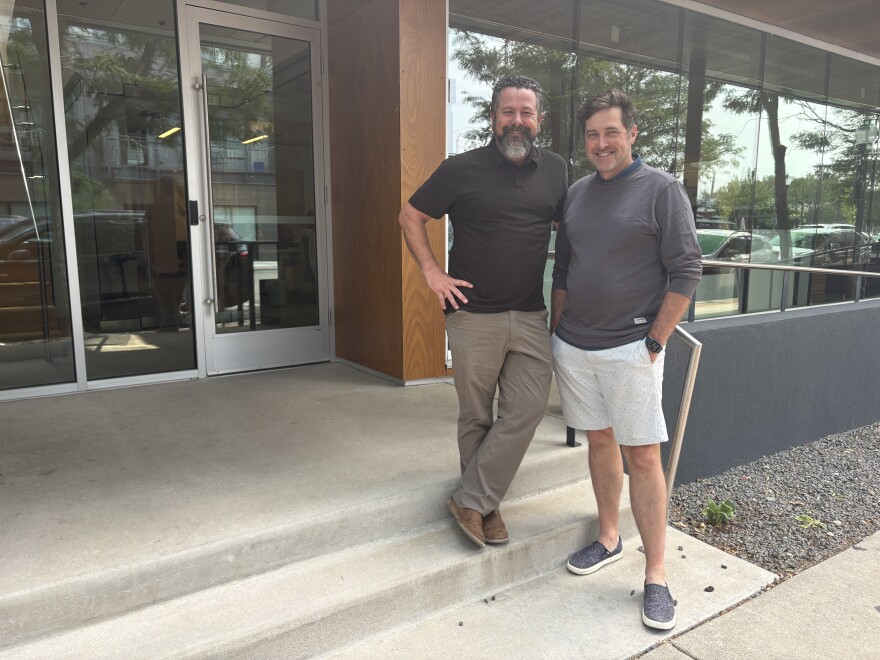 Two men stand in front of an office building.
