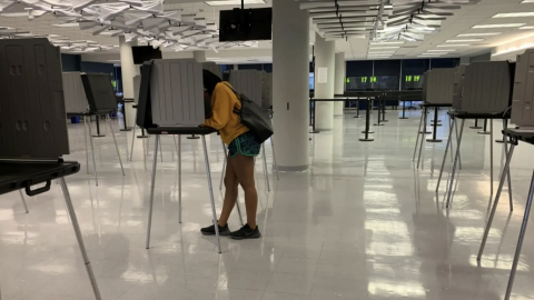 a woman in an otherwise empty polling place leans into a voting booth 