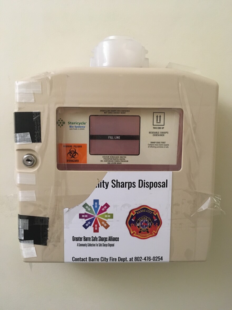 A beige box mounted on a wall with the words "sharps disposal" on it.